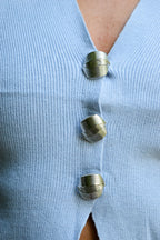 Close-up of a light blue ribbed knit cardigan with three metallic spiral buttons.