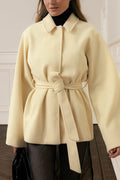 Woman wearing a light yellow coat with a belt in an indoor setting